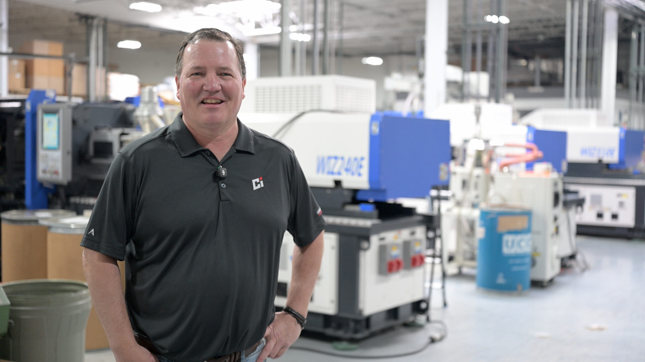 Des Paden standing on the Crestwood Industries shop floor next to injection molding machines
